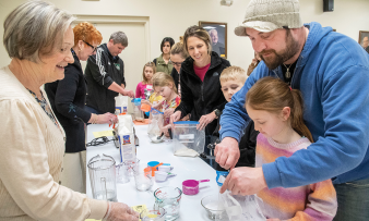 Andy Lang, right, and his daughter Sage, 8, both of Beaverton, place ingredients into a plastic bag to make dough for bread. Volunteer catechist Marabeth Holsinger, left, assists with the process for the Families Forming Disciples class on March 19. 