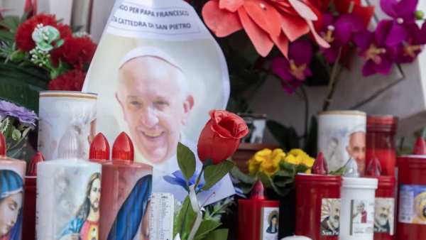 Votive candles and flowers are seen at the base of a statue of St. John Paul II outside Rome's Gemelli hospital March 6, 2025