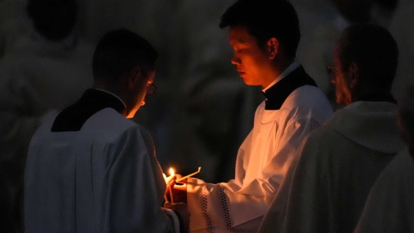 Concelebrant priests light candles from the paschal flame at the start of Easter Vigil Mass in St. Peter’s Basilica at the Vatican April 19, 2025.